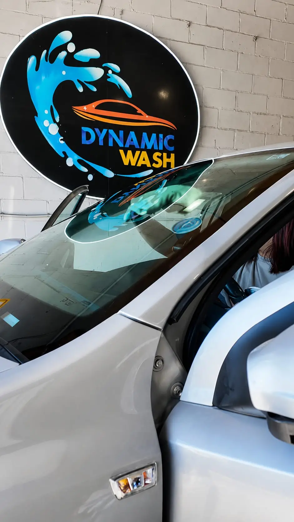 Coche en las instalaciones de Dynamic Wash junto al logotipo de la marca