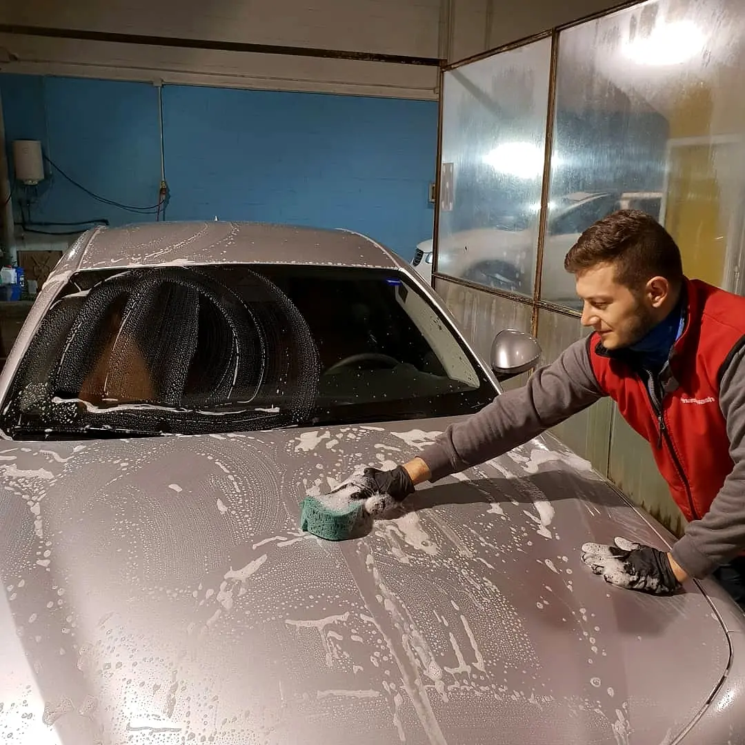 Lavado a mano con esponja y espuma sobre la carrocería de un coche